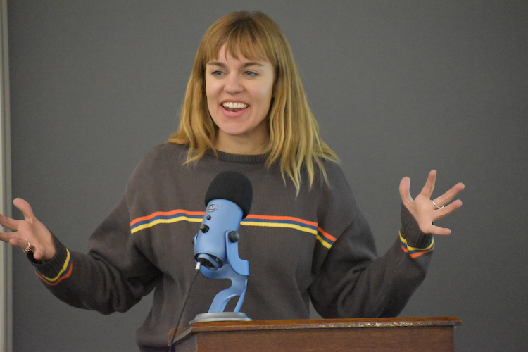 Courtney Kersten smiling and gesturing with hands while speaking at podium with mic
