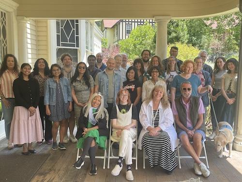 Large group of people smiling and posting at front of historic-looking house